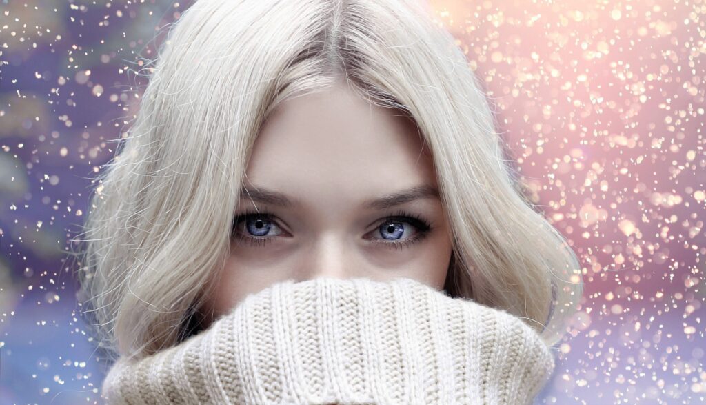 Blonde woman hiding bottom of face behind sweater